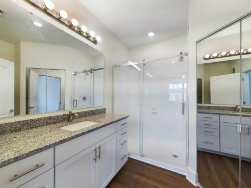 Apartments in Lebanon, IN Modern bathroom with granite countertop, white cabinetry, large mirror, glass-enclosed shower, wooden flooring, and bright overhead lighting.