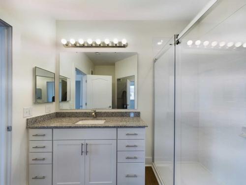 Apartments in Lebanon, IN A modern bathroom featuring a large vanity with a granite countertop and mirror, and a glass-enclosed shower. The vanity has white cabinets and the bathroom has neutral-colored walls.