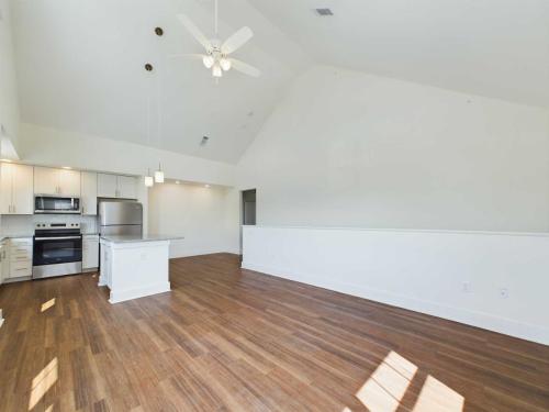 Apartments in Lebanon, IN A spacious, empty living area with wooden flooring and an open kitchen. Kitchen features white cabinetry, an island, stainless steel appliances, and pendant lighting. Ceiling fan is mounted on the high ceiling.