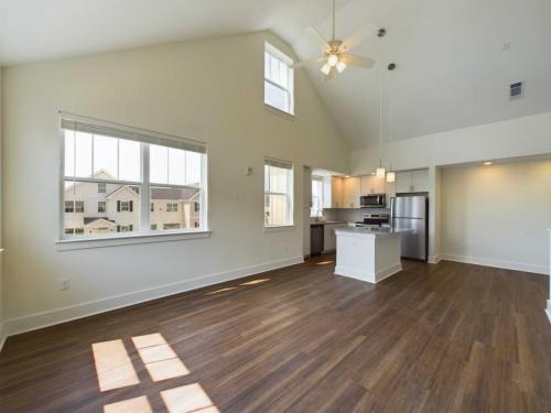 Apartments in Lebanon, IN A modern, unfurnished apartment with an open floor plan featuring a kitchen, living area, high ceilings, and wooden floors. Sunlight streams through large windows. Stainless steel appliances are present.