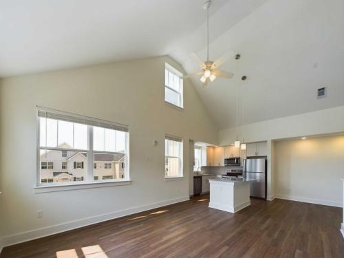 Apartments in Lebanon, IN A modern apartment interior with high ceilings, wood floors, a ceiling fan, large windows, and a kitchen with stainless steel appliances.