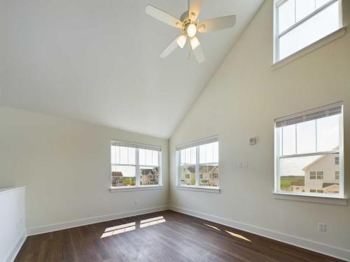 Apartments in Lebanon, IN A spacious room with three large windows, wood flooring, and a ceiling fan. The walls are painted white and sunlight illuminates the room.