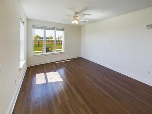 Indiana, Boone County, Lebanon Apartments for rent An empty room with wooden floors, a ceiling fan, and large windows letting in natural light. White walls and a small built-in window seat are visible. See all available apartments for rent at Hickory Cottages in Indiana Boone County Lebanon, Hickory Cottages has rental units ranging from 664-1420 sq ft