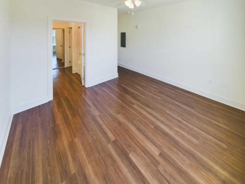 Indiana, Boone County, Lebanon Apartments for rent Empty room with light-colored walls and a ceiling fan. The floor has wide, dark wood planks. A doorway opens to a hallway leading to additional rooms. Natural light enters from a window. See all available apartments for rent at Hickory Cottages in Indiana Boone County Lebanon, Hickory Cottages has rental units ranging from 664-1420 sq ft