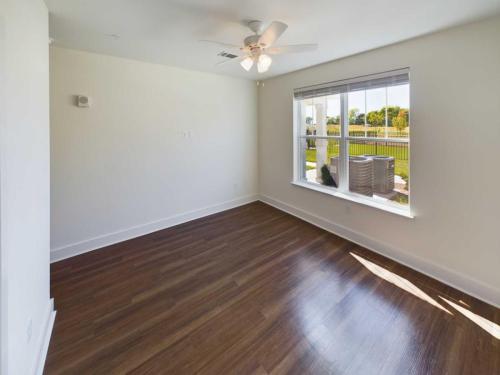 Indiana, Boone County, Lebanon Apartments for rent Empty room with wooden floor, white walls, a ceiling fan, and a large window overlooking a garden with trees and a lawn. See all available apartments for rent at Hickory Cottages in Indiana Boone County Lebanon, Hickory Cottages has rental units ranging from 664-1420 sq ft