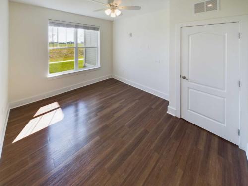 Indiana, Boone County, Lebanon Apartments for rent An empty room with wooden flooring, a ceiling fan, a window with sunlight streaming in, and a closed white door. See all available apartments for rent at Hickory Cottages in Indiana Boone County Lebanon, Hickory Cottages has rental units ranging from 664-1420 sq ft