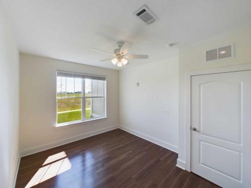 Indiana, Boone County, Lebanon Apartments for rent Empty room with white walls, a ceiling fan, large window with blinds, wooden floor, and a closed white door. See all available apartments for rent at Hickory Cottages in Indiana Boone County Lebanon, Hickory Cottages has rental units ranging from 664-1420 sq ft