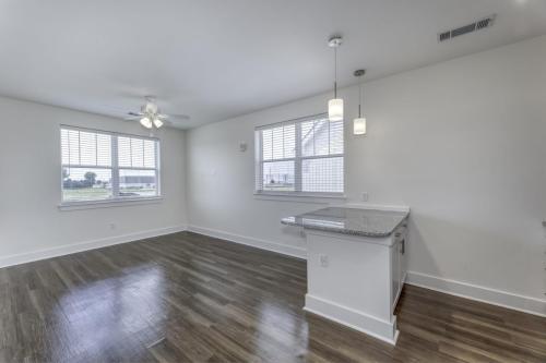 Apartments in Lebanon, IN An empty room with large windows, ceiling fan, hardwood floors, and a small kitchen island with two hanging lights.