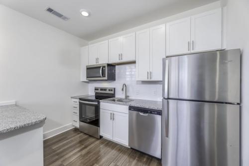 Apartments in Lebanon, IN Modern kitchen with white cabinets, stainless steel appliances including a microwave, oven, refrigerator, and dishwasher. Dark wood flooring and gray granite countertops are also visible.