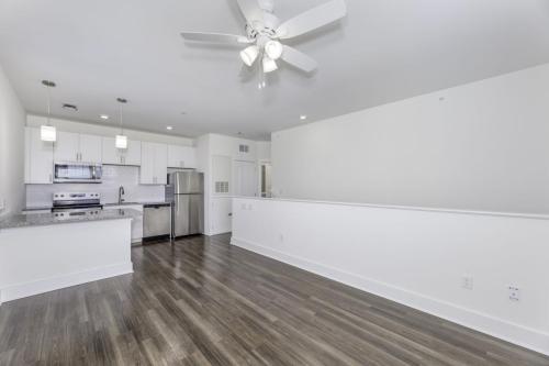 Apartments in Lebanon, IN Modern kitchen and living space with white cabinetry, stainless steel appliances, hardwood flooring, ceiling fan, and pendant lighting. The area is clean and spacious, featuring an open floor plan.