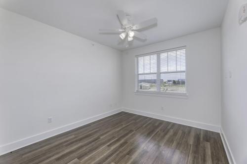 Apartments in Lebanon, IN An empty room with white walls, a ceiling fan, hardwood floors, and a window with white blinds overlooking an outdoor scene.