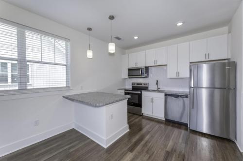 Apartments in Lebanon, IN Modern kitchen with stainless steel appliances, white cabinets, granite countertops, and wood flooring. Features an island with two pendant lights and a window with blinds.