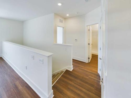 Apartments in Lebanon, IN Upstairs hallway with white walls, recessed lighting, and wooden flooring in one of the Apartments For Rent in Lebanon Indiana. Features a staircase with a white handrail and a door to a room on the right.