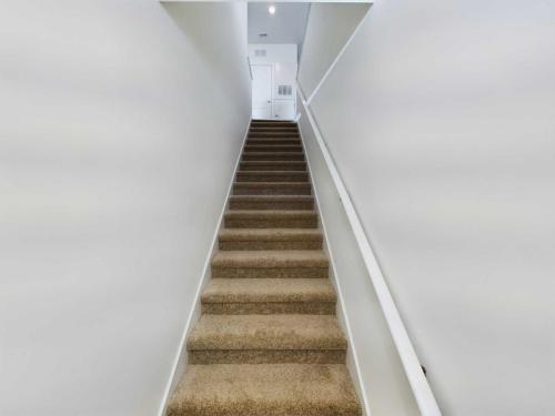 Apartments in Lebanon, IN A carpeted staircase with a white handrail on the right side leads upward to a white door in the brightly lit hallway of one of the finest apartments for rent in Lebanon, Indiana.