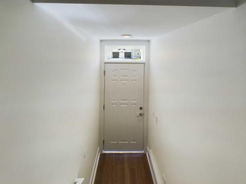 Apartments in Lebanon, IN A narrow hallway with white walls and a wooden floor leads to a closed door with a small rectangular window above it, typical of charming apartments for rent in Lebanon, Indiana.