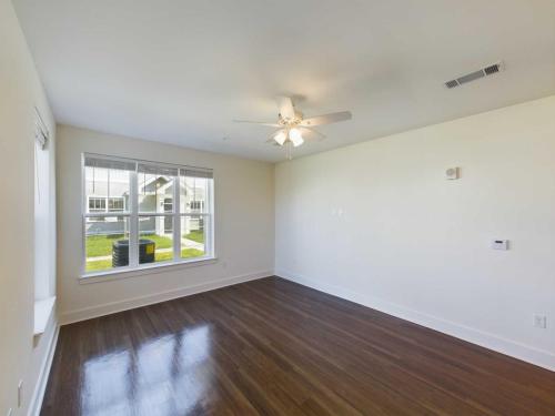 Indiana, Boone County, Lebanon Apartments for rent Empty room with wooden floor, large window, ceiling fan, and white walls. Window view shows a green lawn and residential buildings. See all available apartments for rent at Hickory Cottages in Indiana Boone County Lebanon, Hickory Cottages has rental units ranging from 664-1420 sq ft