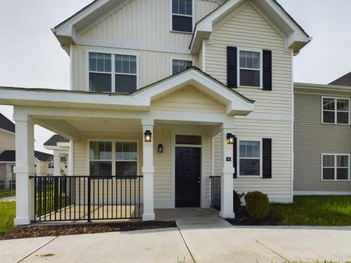 Apartments in Lebanon, IN A modern two-story house with white siding, black shutters, and a covered front porch. The porch has a black metal railing and two wall-mounted lights on either side of the front door.