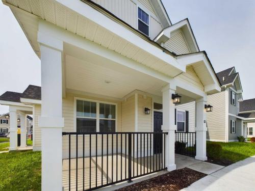 Apartments in Lebanon, IN A two-story house with beige siding and a covered front porch featuring white pillars and black railings. The yard is partially visible with green grass and a paved walkway.